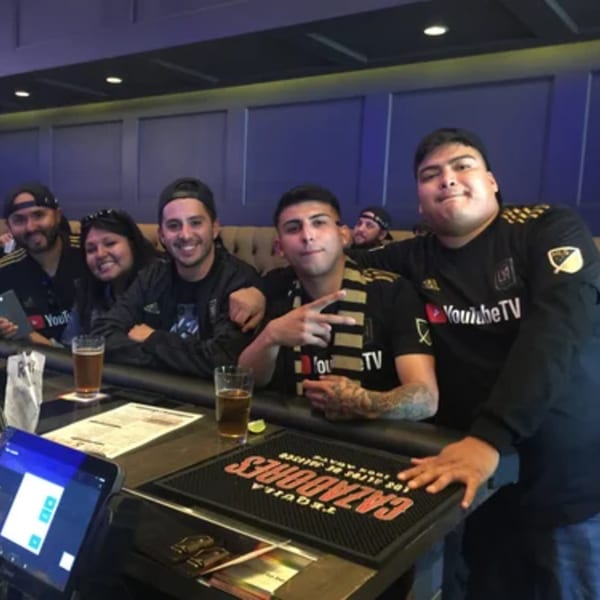 Five friends in black shirts and hats enjoying drinks at a bar, with a "Cazadores Tequila" mat.