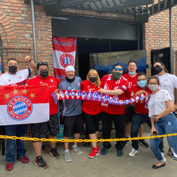 A group of people wearing FC Bayern Munich gear pose with flags and scarves outside R Bar.