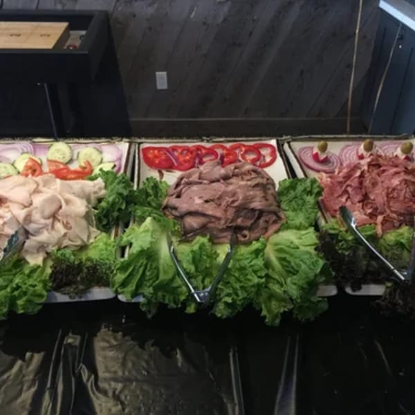 A buffet spread with three trays of deli meats, lettuce, and sliced vegetables.