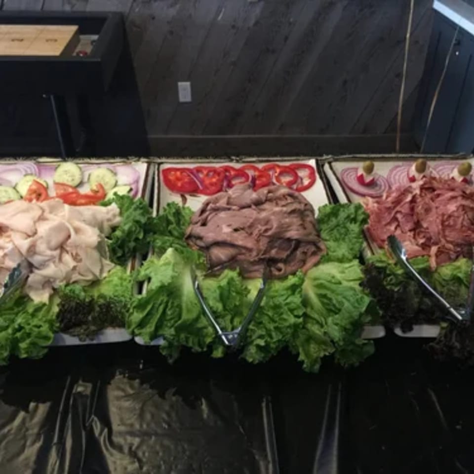 A buffet spread with three trays of deli meats, lettuce, and sliced vegetables.