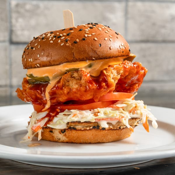 A crispy fried chicken sandwich with coleslaw, tomato, and sauce on a sesame bun.