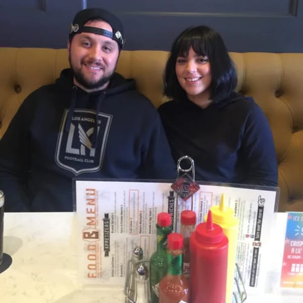 Smiling couple seated at a table with a menu, condiments, and drinks at R Bar.