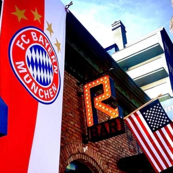 R Bar exterior with a large illuminated 'R' sign, FC Bayern flag, and American flag.