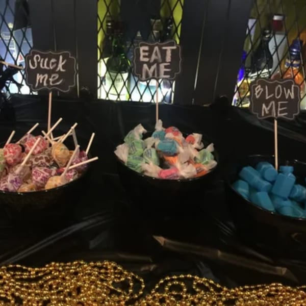 Three bowls of candy with playful signs "Suck Me," "Eat Me," and "Blow Me" at R Bar.