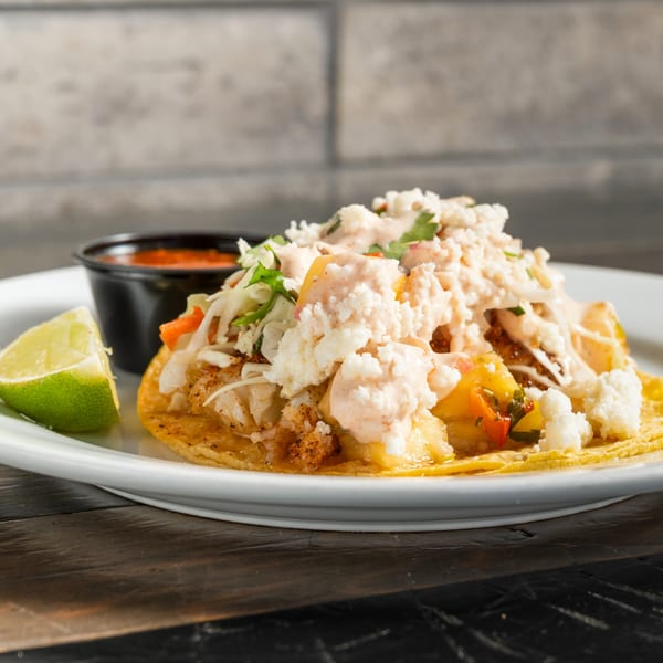 R Bar's fish taco with white sauce, crumbled cheese, and a lime wedge on a white plate.