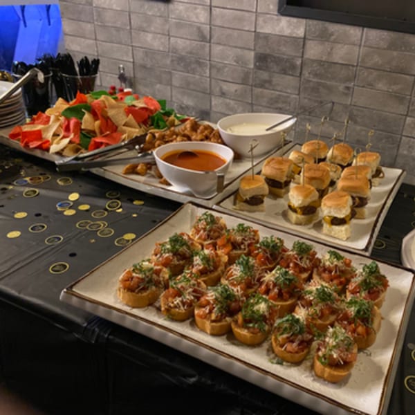 A buffet spread with bruschetta, mini cheeseburger sliders, tortilla chips, and dips at R Bar.