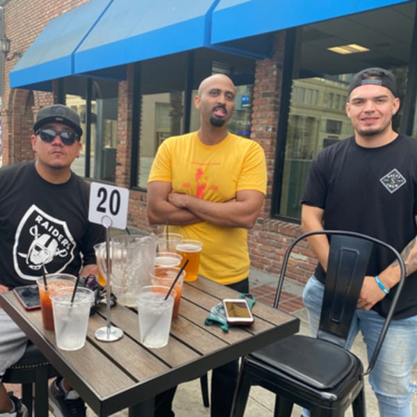 Three men enjoying drinks at an outdoor patio table at R Bar.