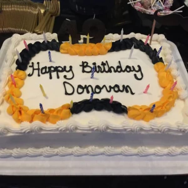 White birthday cake with "Happy Birthday Donovan" in black icing, surrounded by colorful candles.