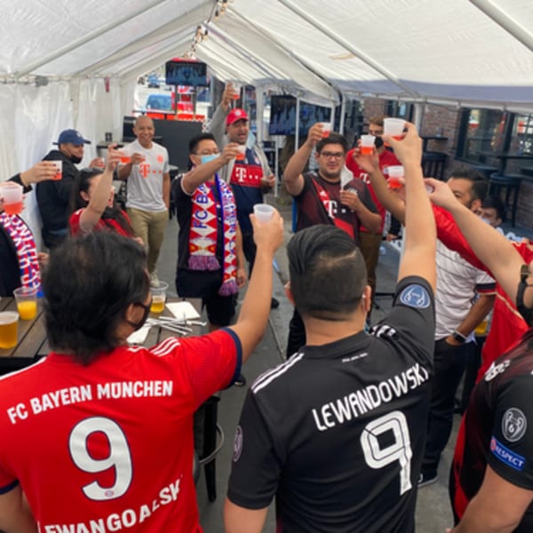 A group of people in soccer jerseys raising drinks in a toast under a white tent.