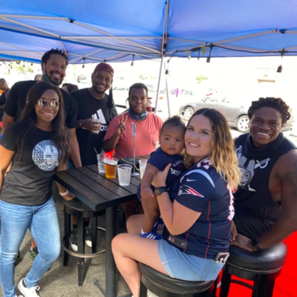 A group of friends and a baby enjoying drinks and conversation under a blue tent at R Bar.