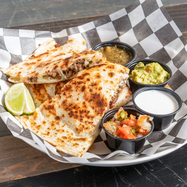 R Bar's beef quesadillas with lime, salsa, guacamole, and sour cream on a checkered paper.
