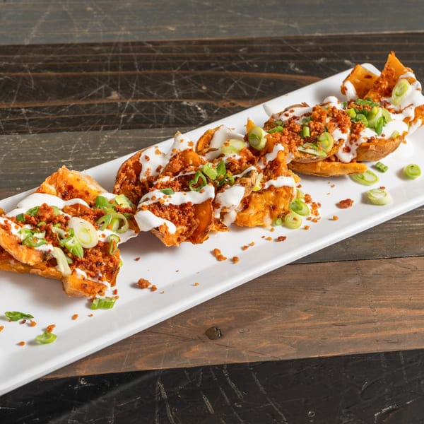 R Bar potato skins topped with sour cream, bacon bits, and green onions on a white platter.