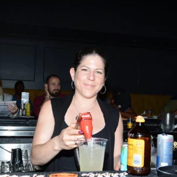 A smiling R Bar bartender pours a drink from a soda gun into a plastic cup.