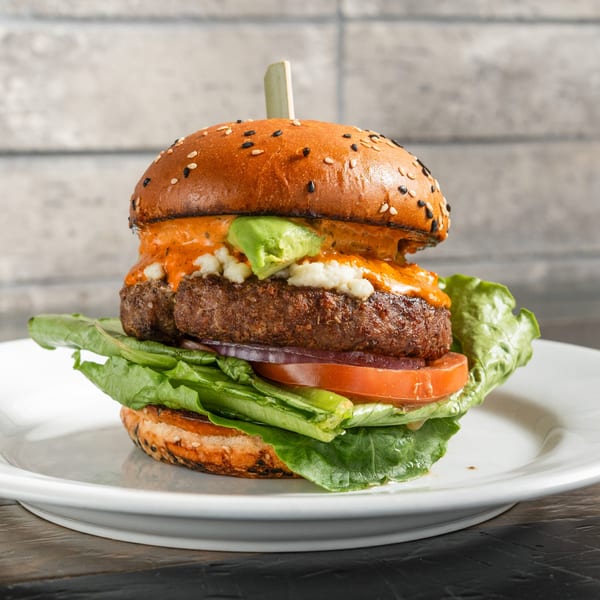 A R Bar burger with a thick patty, lettuce, tomato, avocado, and special sauce on a sesame bun.