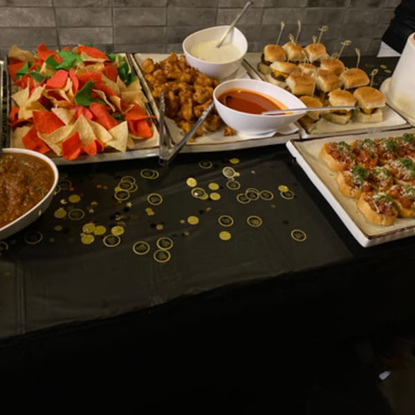 A buffet spread with chips and salsa, fried appetizers, mini burgers, and bruschetta on a black tablecloth.