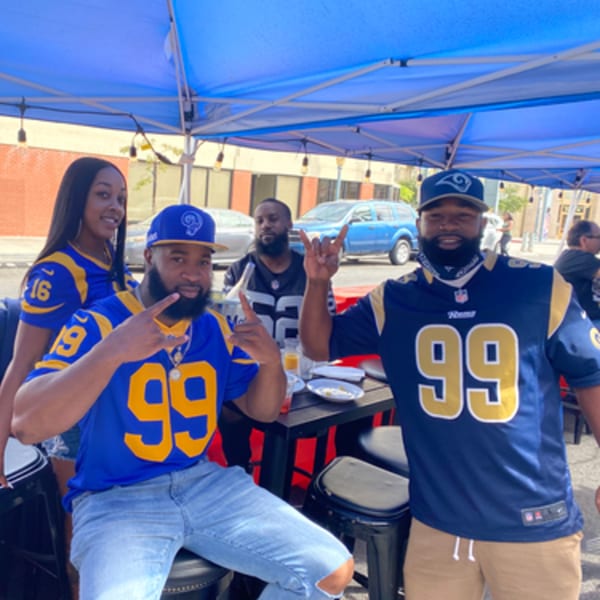 Four people in blue and gold jerseys pose under a blue tent at an outdoor bar.