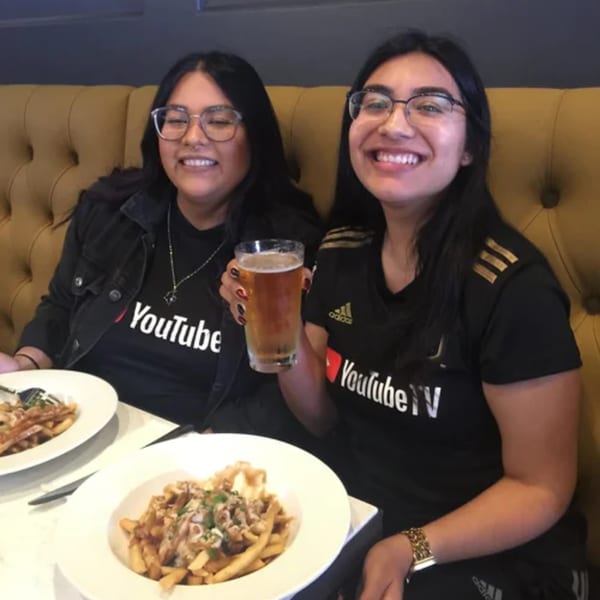 Two smiling women in YouTube shirts enjoy R Bar's loaded fries and a beer.